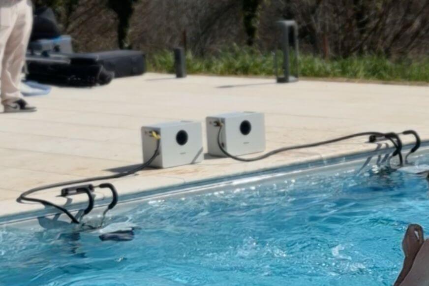 iGarden Swim Jet X Series Akku-Pack steht außerhalb des Pools am Poolrand und ist mit der Gegenstromanlage verbunden.